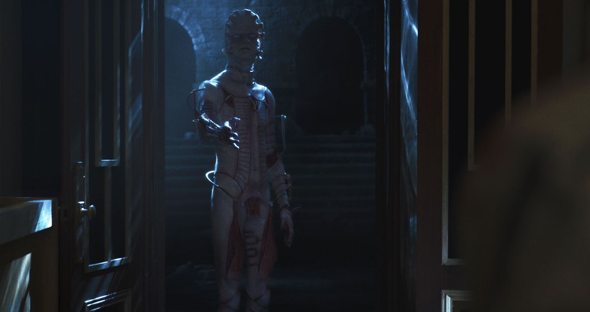 A cenobite with flayed skin and a flat head enters from the darkness in a mansion room