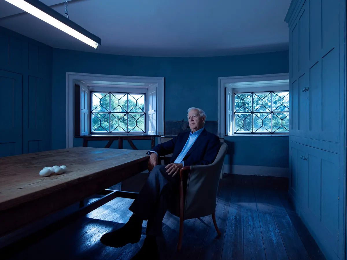 John le Carré sits in a chair next to a set of eggs on a wooden table in The Pigeon Tunnel.