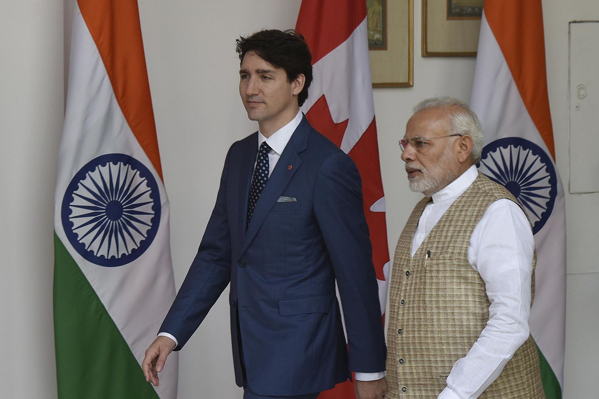 Modi and Trudeau walking in front of Canadian and Indian flags.