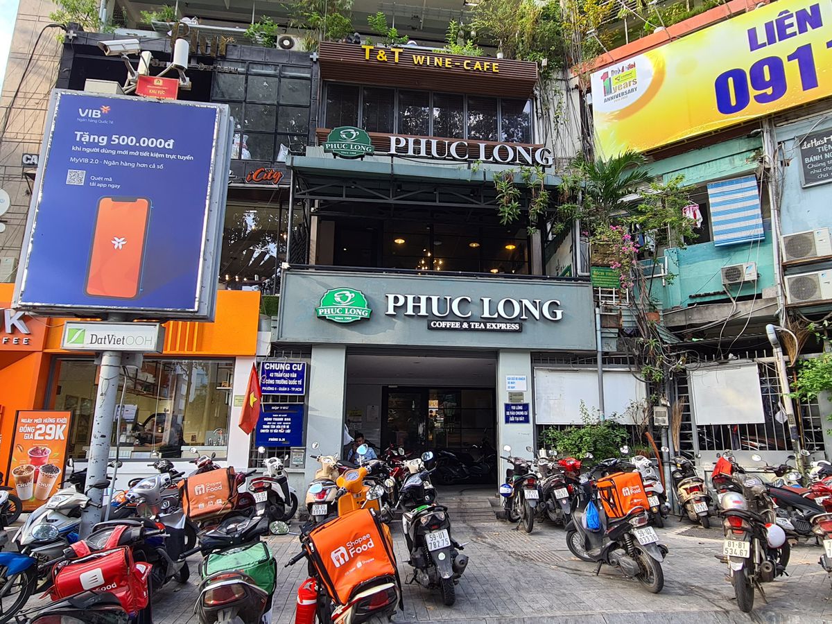 A cafe exterior set among a flurry of other businesses and surrounded by mopeds.