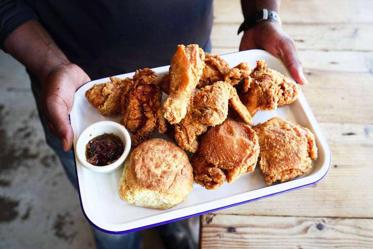 Greg Gatlin holding a tray of fried chicken, a biscuit, and a dipping sauce.
