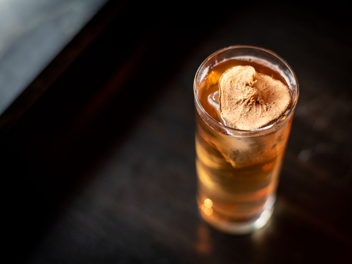 A aerial view of a highball topped with a dried apple slice against a black background. 