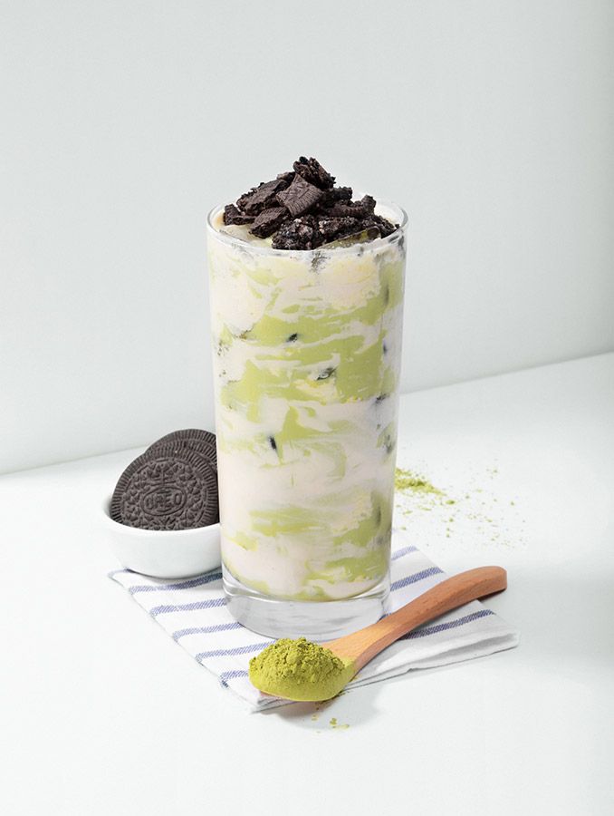A tall photo of a green, white tea drink with oreos on top.
