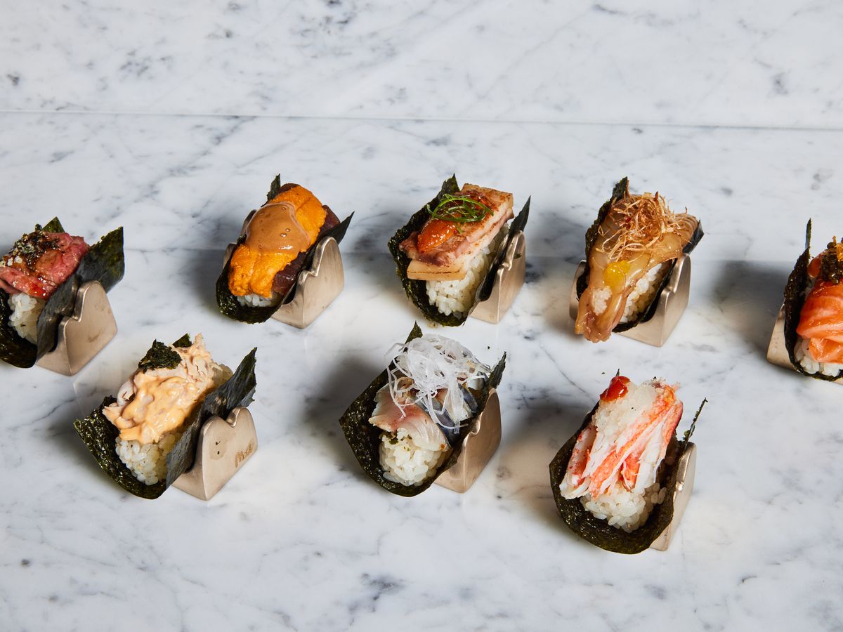 A selection of handrolls topped with different cuts of fish, laid out on a marble background.