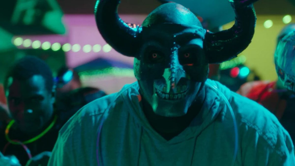A man wearing a demon mask stands in a crowd of people in The First Purge.