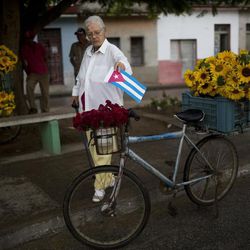 In this Wednesday, Nov. 30, 2016 photo, Concepcion Hernandez places a Cuban flag on a bicycle used by a flower vendor in downtown Camaguey in eastern Cuba. In the cities some of the ceremony for the late Fidel Castro is undercut by grumbling about Cuba’s autocratic government, inefficient bureaucracy and stagnant economy, but the outpouring feels most heartfelt in eastern Cuba, the region his ashes are crossing on Friday. 