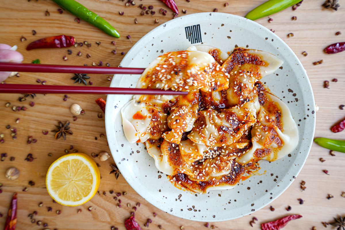 Overhead, a bowl of sauced dumplings with one being picked up by chopsticks.