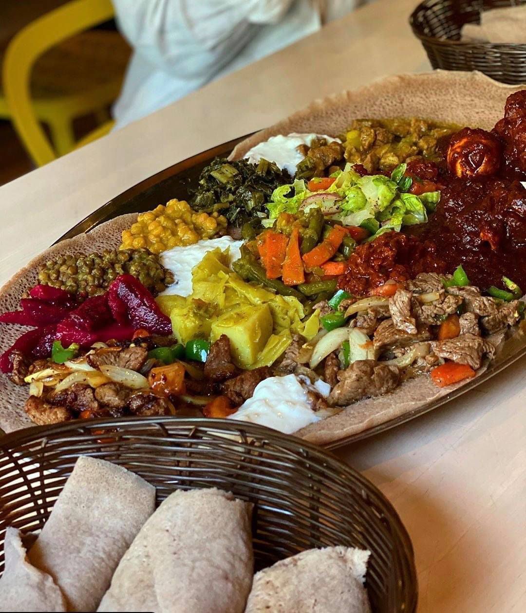A colorful plate of Ethiopian dishes with a side basket of rolled injera bread