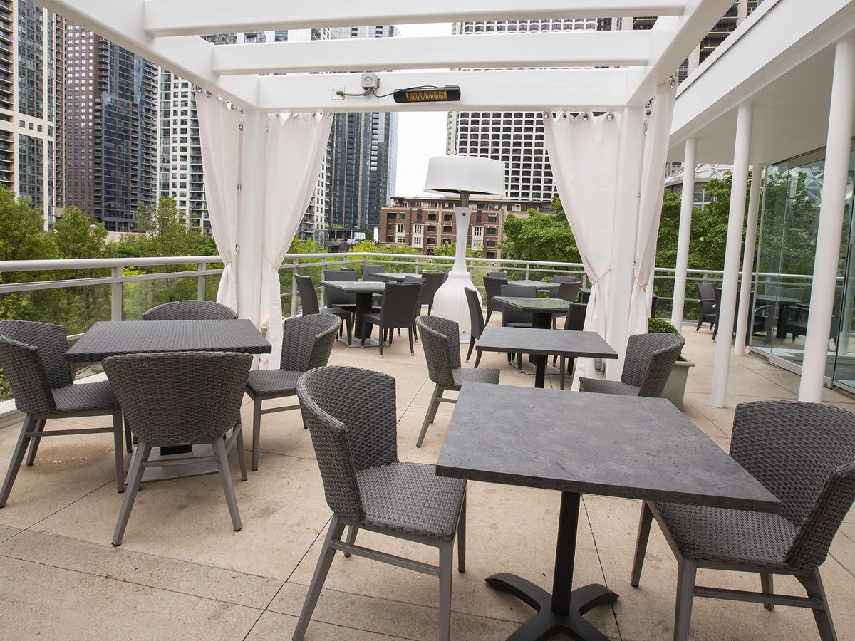 Cabanas over tables on a rooftop overlooking trees and downtown Chicago buildings.