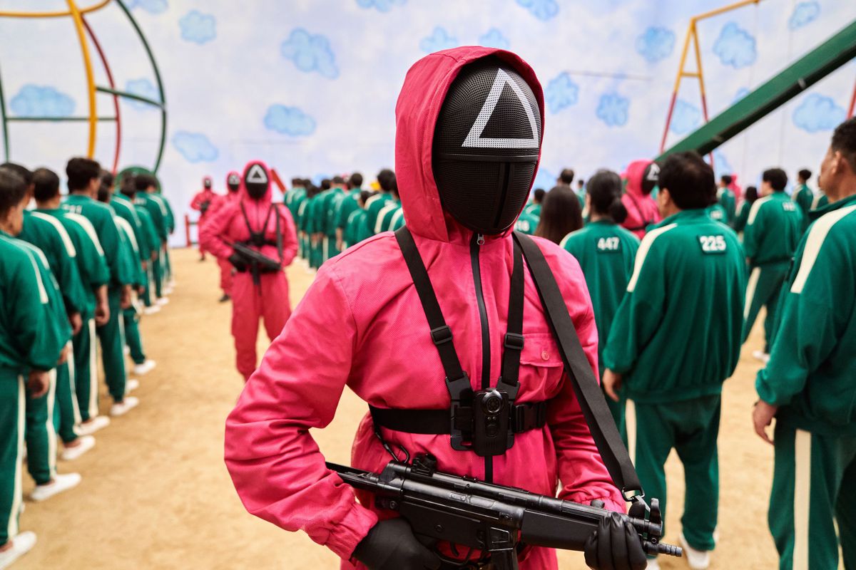 A group of masked men in pink jumpsuits brandishing assault rifles in Squid Game.