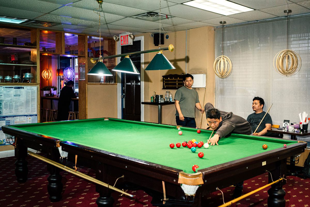 A man lines up a combination shoot while two men stand next to the snooker table watching on.