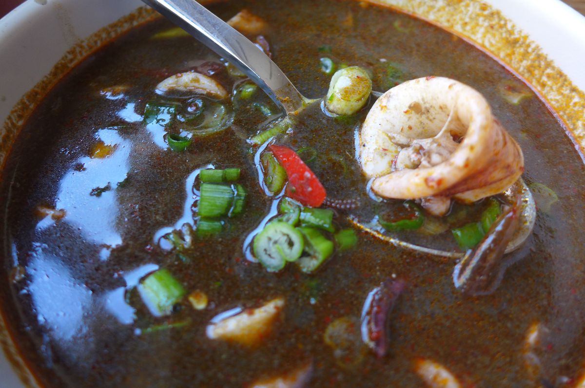 A very dark broth with a squid ring held above it in a spoon.