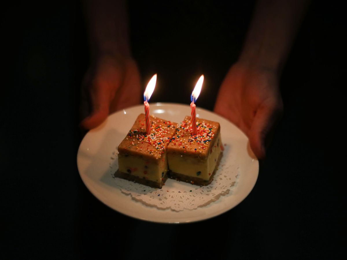 Two ice cream sandwich squares with colorful sprinkles and birthday candles that are lit.