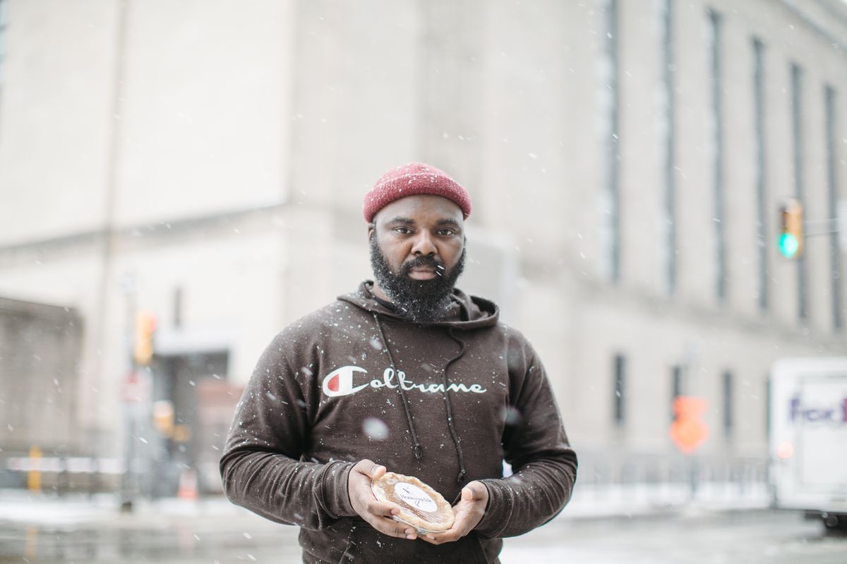 A man stands in the snow on a street corner holding a small pie