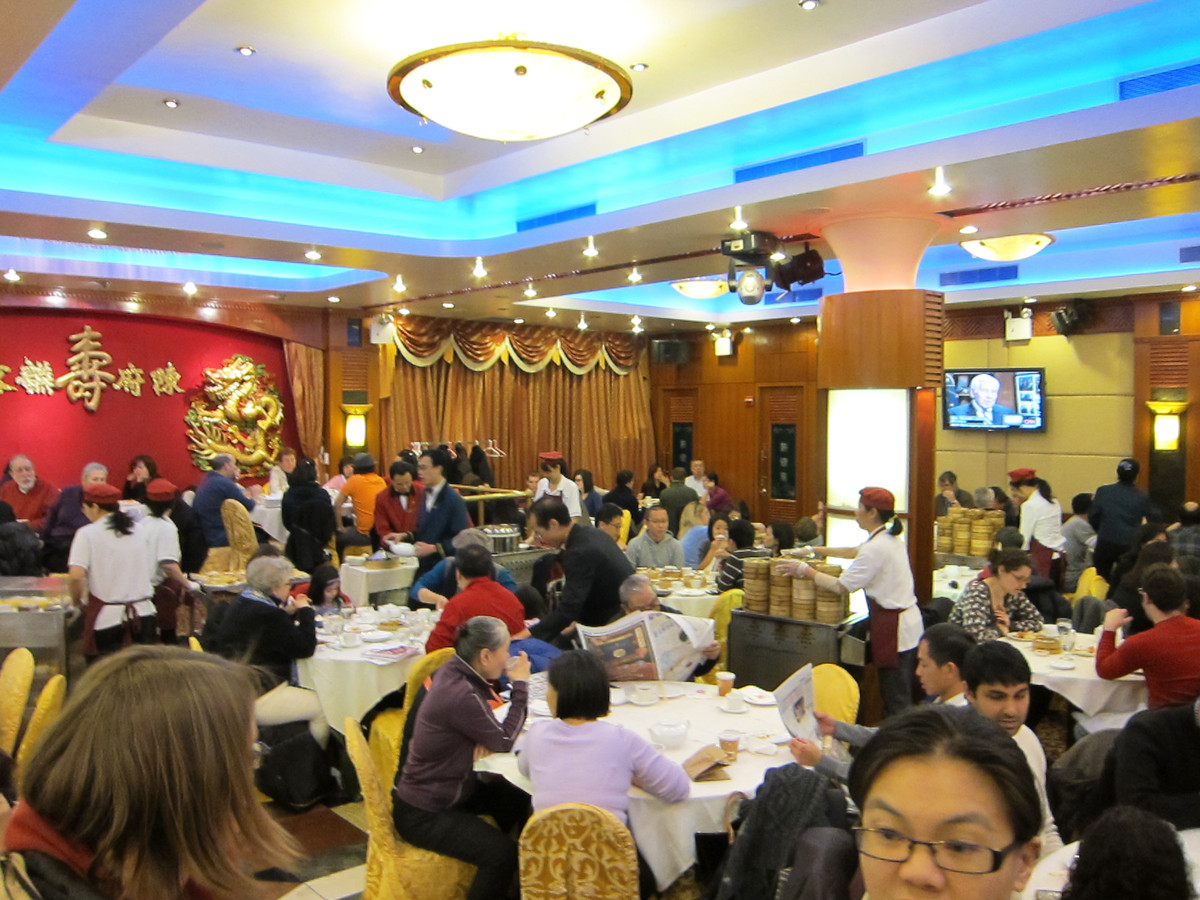 A Chinese banquet hall with round tables with guests seated and roving dim sum carts.