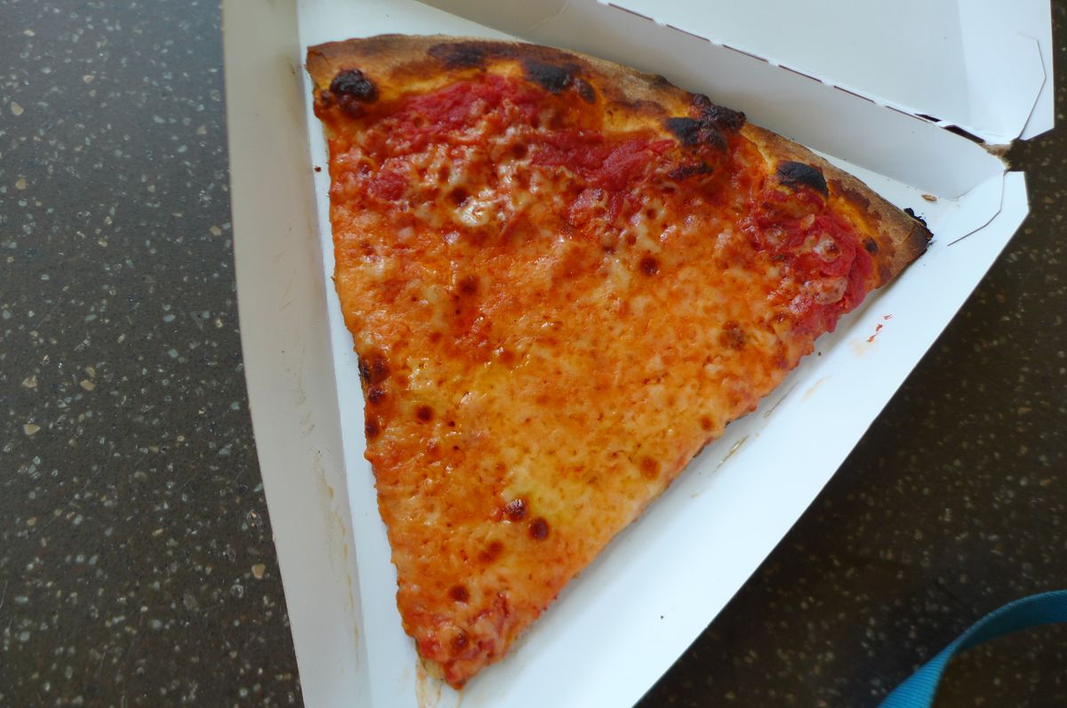A wedge shaped slice of pizza with bubbles in the cheese and a charred circumferential crust.