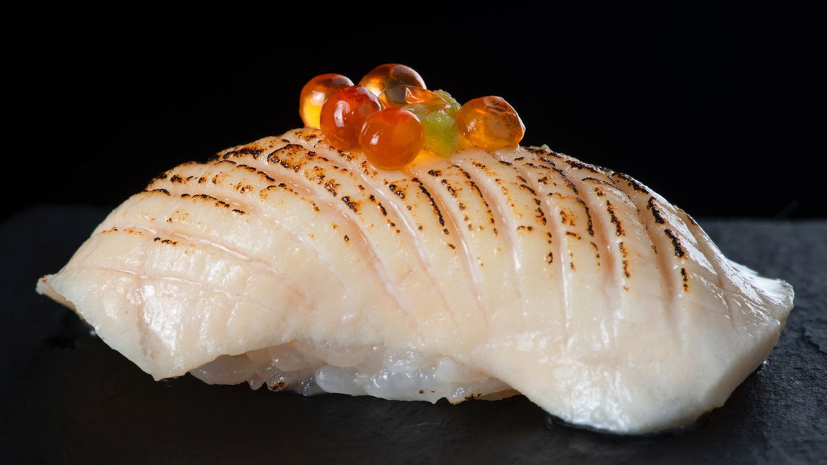 A piece of nigiri made with seared white fish topped with salmon roe.