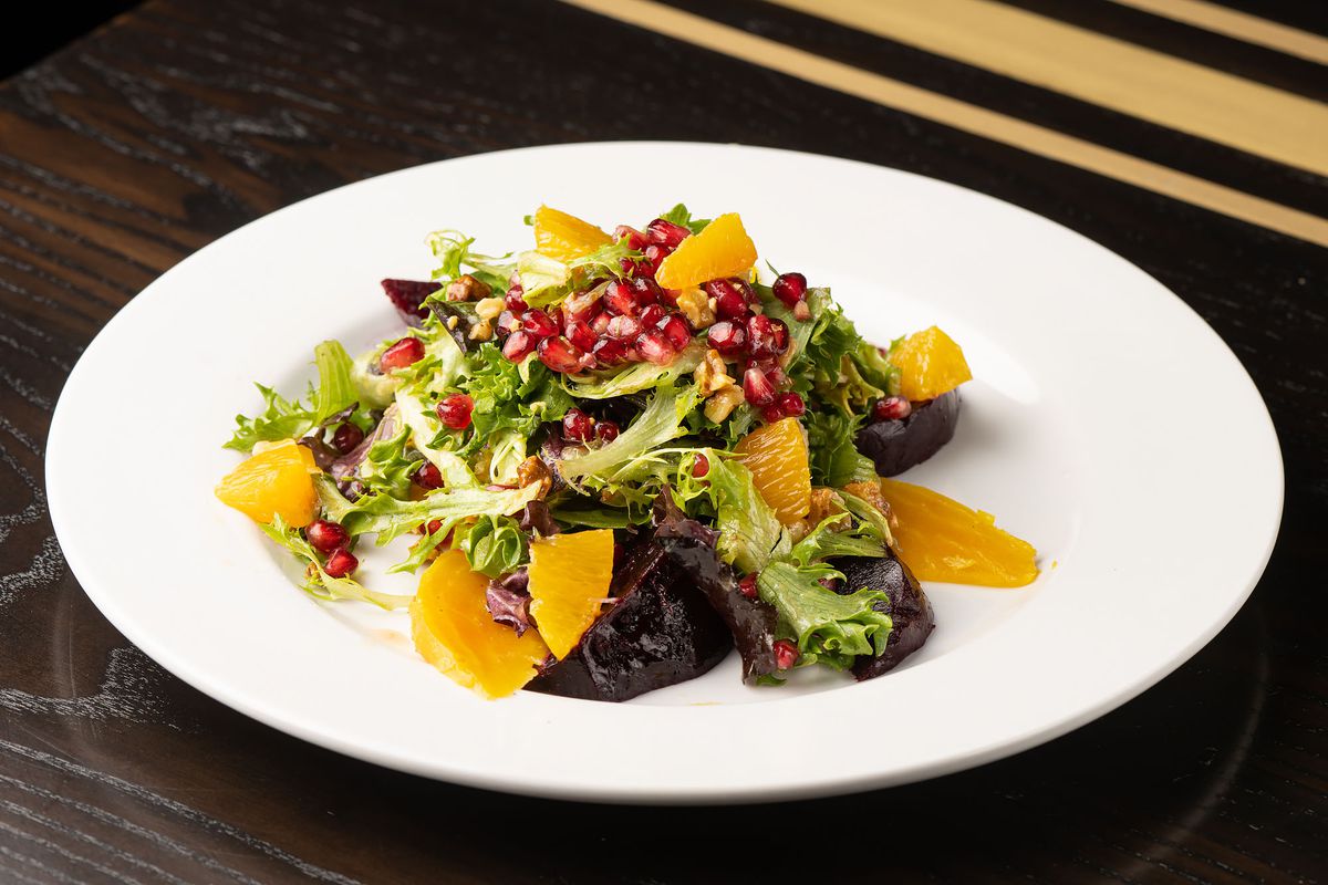 A tilted angle of a greens salad with golden and purple beets, orange and pomegranate.