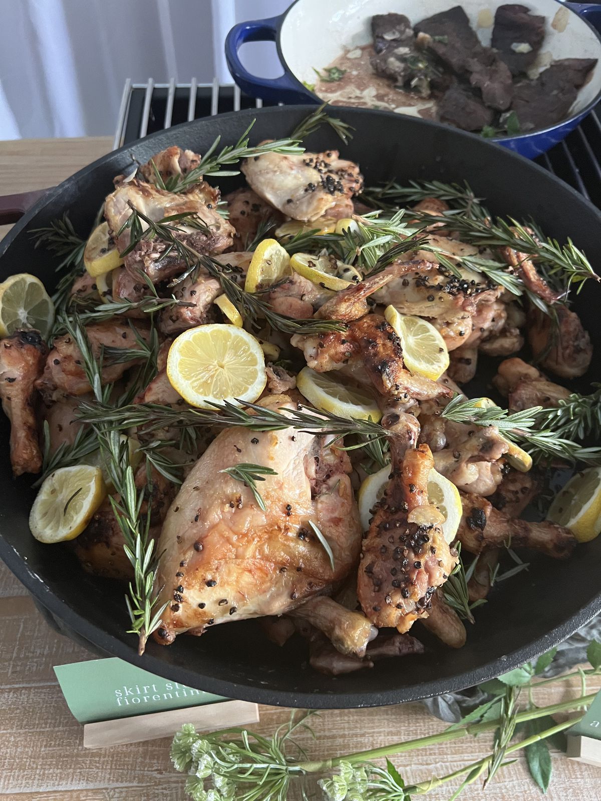 A bowl holds various pieces of roast chicken dressed up with sprigs of rosemary and lemon slices.