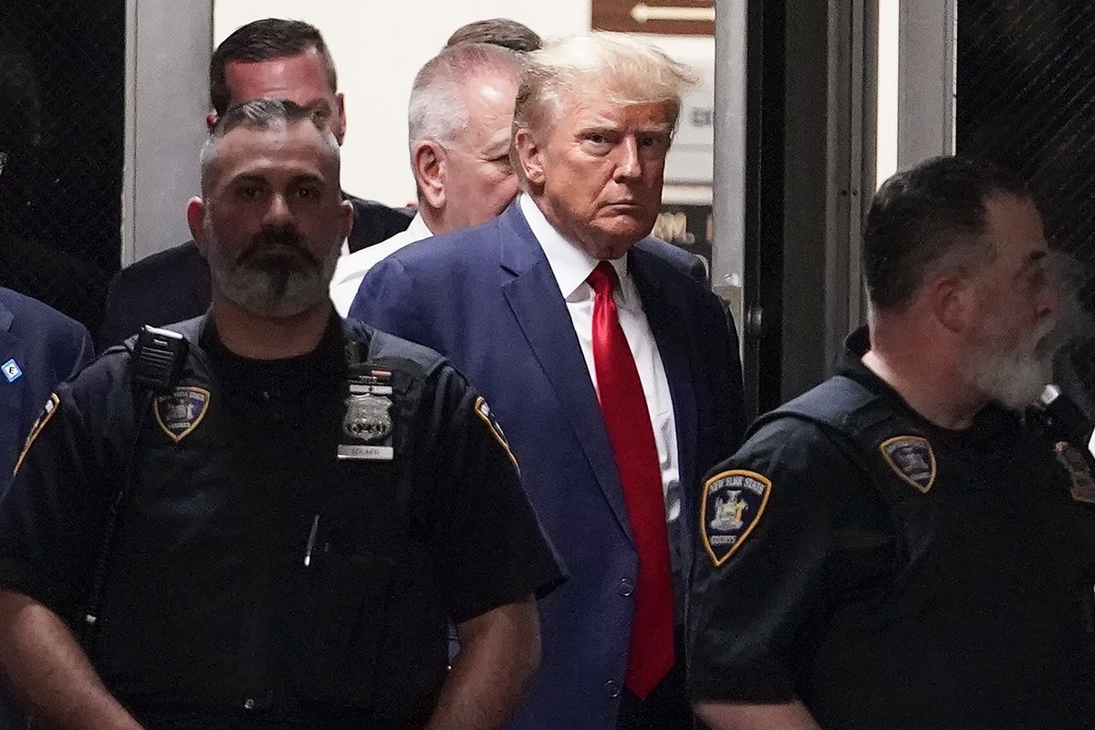 Trump, in a blue suit, white shirt, and red tie frowns amid a circle of uniformed police officers.