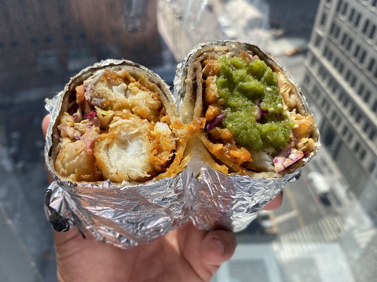 Two halves of a burrito with pieces of crispy, fried fish and a splash of green salsa.
