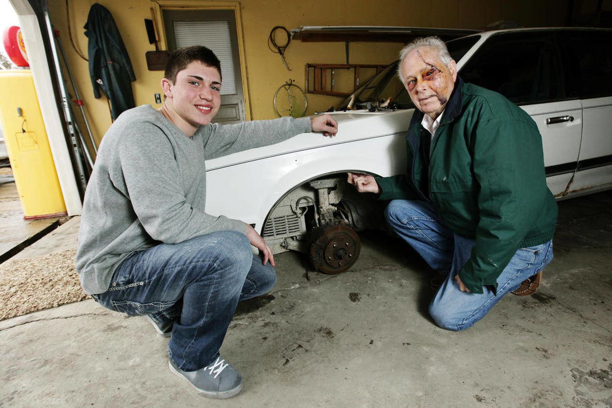 In this Feb. 22, 2012 photo, fifteen-year-old Austin Smith poses with his grandfather Ernie Monhollen next to the 1991 Buick Century that had fallen on him while the pair worked on the car in Monroe, Mich. When the car slipped off the blocks and fell on t