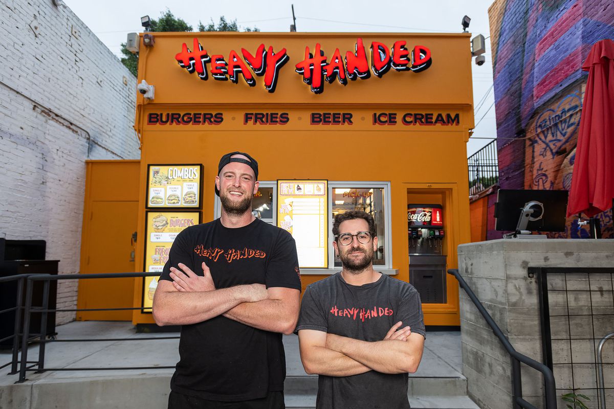 Two men in black t-shirts stand in front of a burger window at Heavy Handed.