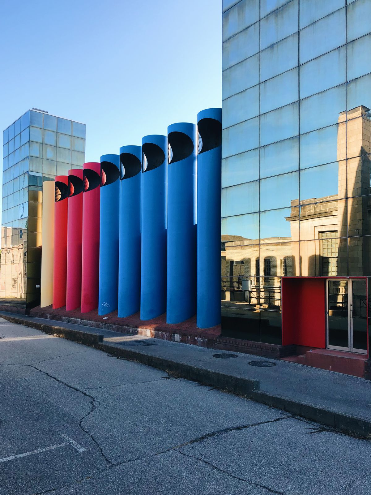 Two all-glass buildings encase eight tall columns, three red and five blue.