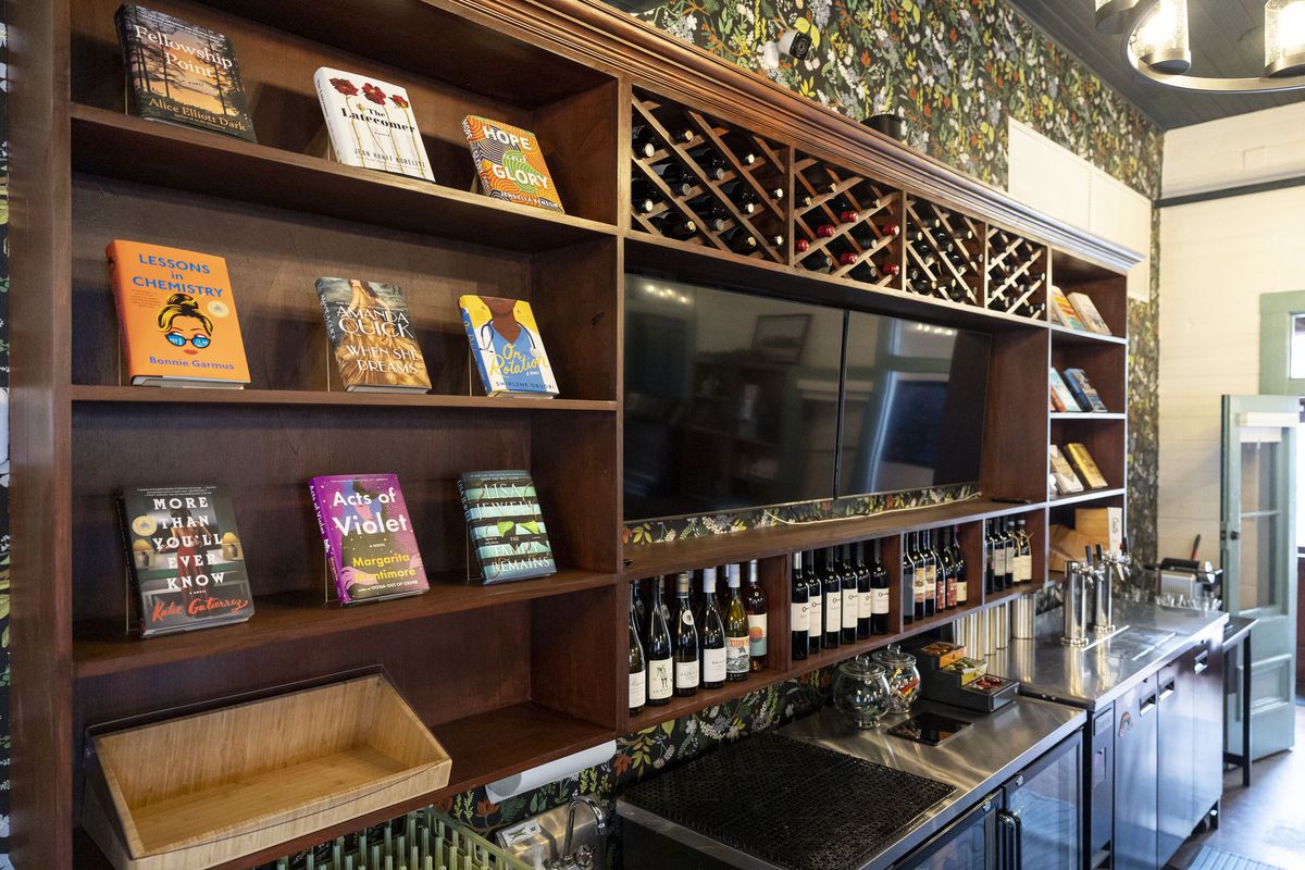 A wooden hanging wine bar with books on shelves, a television screen, and criss-crossed shelves with bottles of wine.