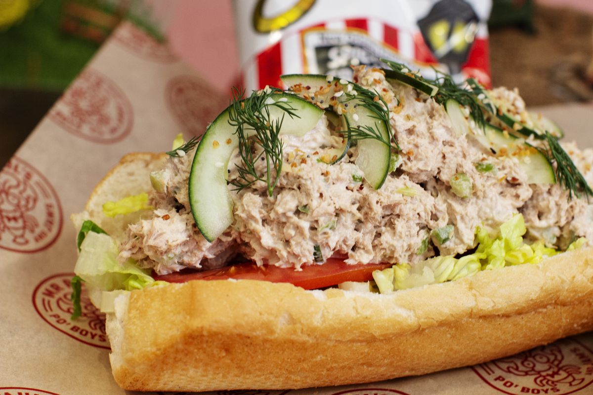 A po’ boy sandwich heaped with tuna salad on a brown piece of paper. 