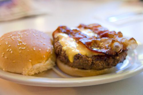 An open-faced cheeseburger rests on a plate, topped with bacon