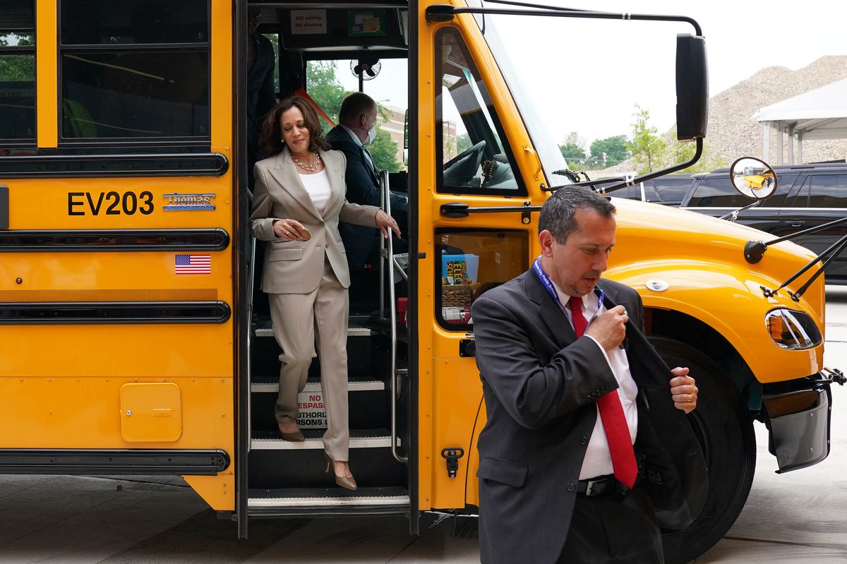 Vice President Kamala Harris, wearing a tan suit, steps out of a large yellow electric school bus during a tour in Falls Church, Virginia, on May 20, 2022. 