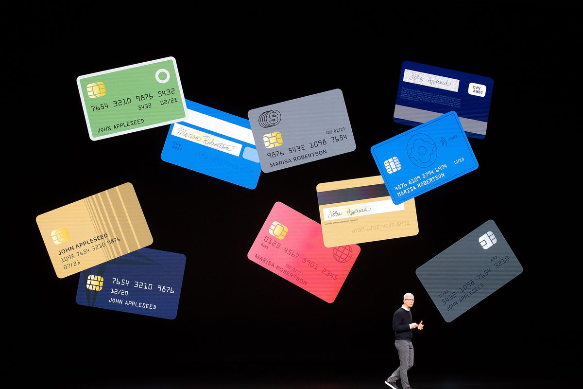 Apple CEO Tim Cook onstage at the Apple Card launch event with a wall-sized screen behind him displaying credit cards.