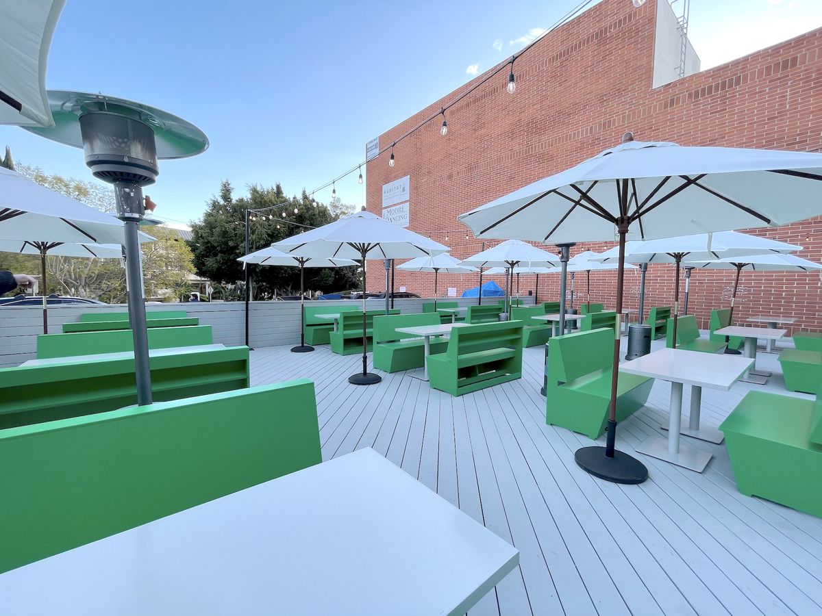 An outdoor patio with bright green booths and string lights during COVID.