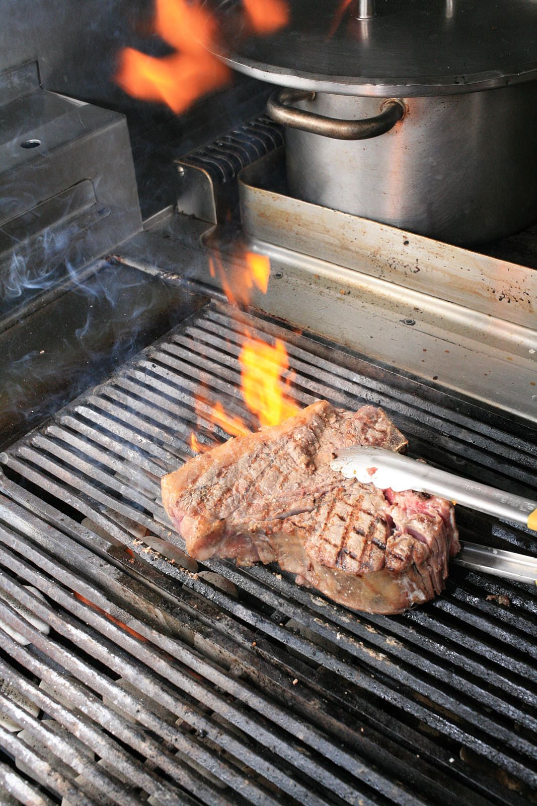 A beef steak on grill bars, flames licking it from below.