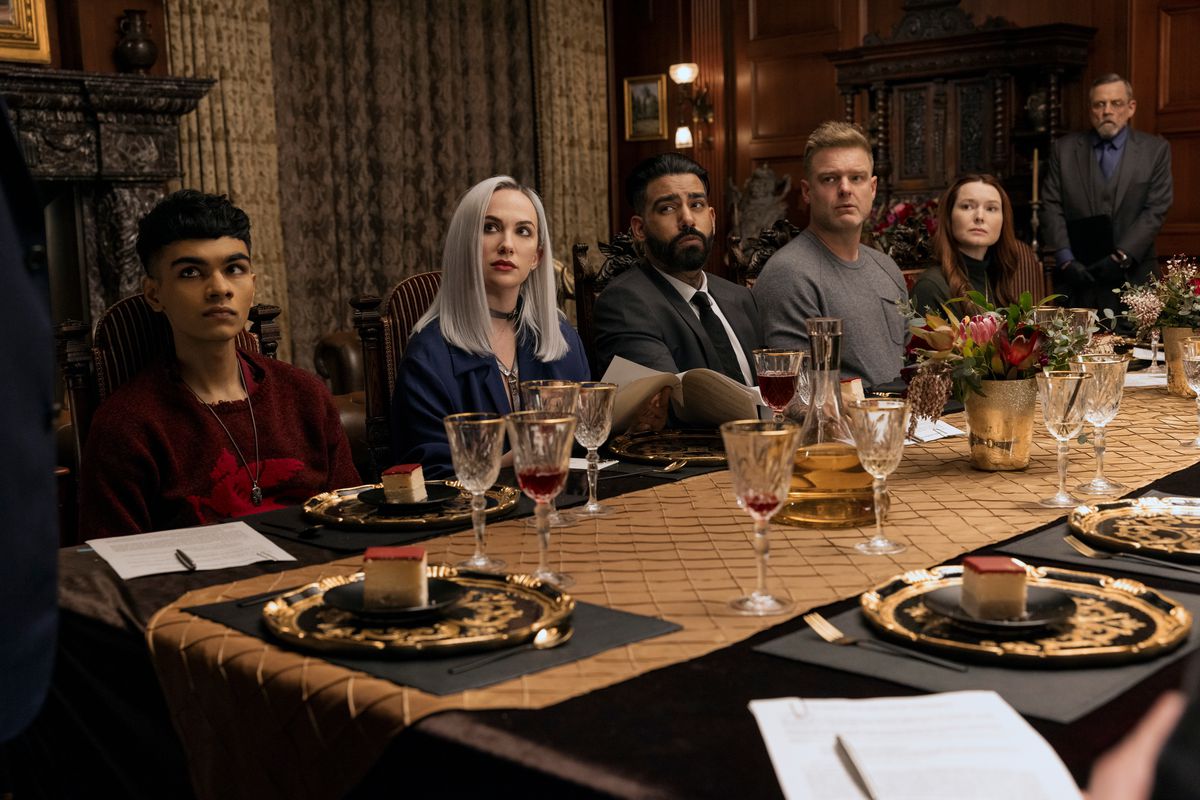 Sauriyan Sapkota, Kate Siegel, Rahul Kohli, Matt Biedel, Samantha Sloyan sit around a table while Mark Hamill stands behind them in Fall of the House of Usher.