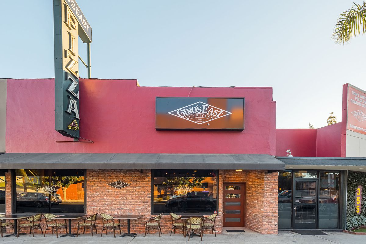 The exterior of a red pizza building with tables.