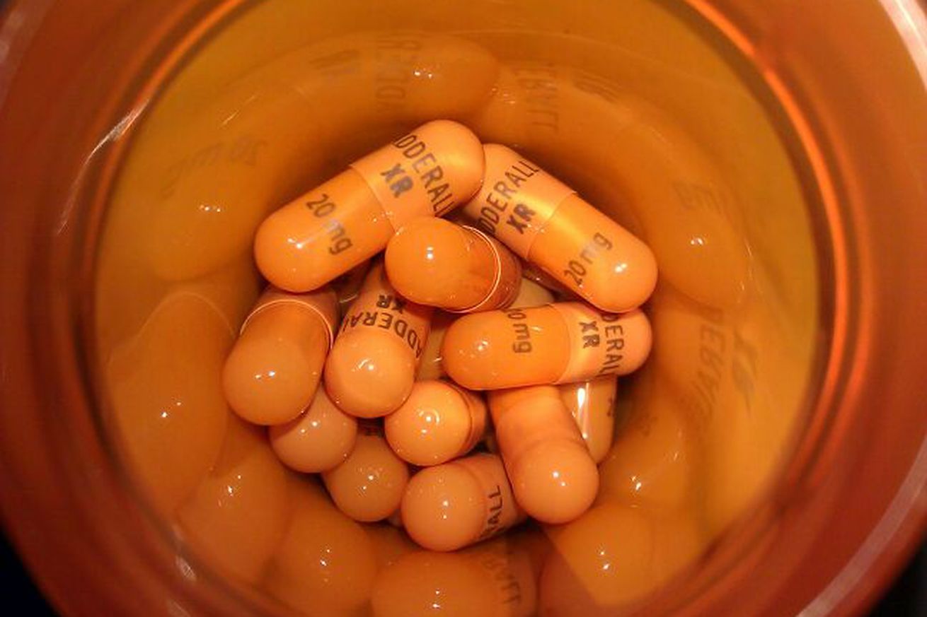 A top-down view of an orange pill bottle filled with Adderall capsules.