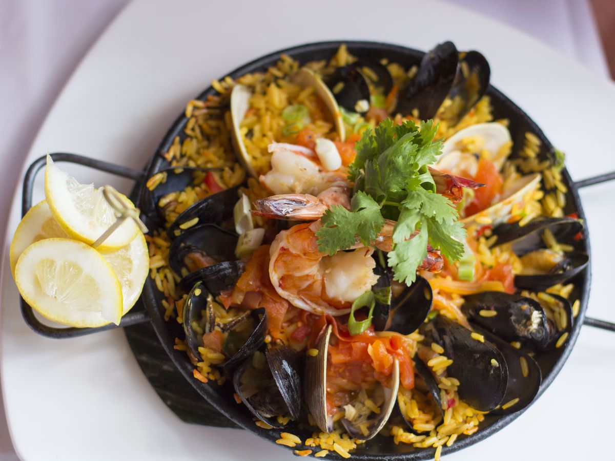 A black, round dish filled with yellow rice and seafood, with a lemon wedge on the side.