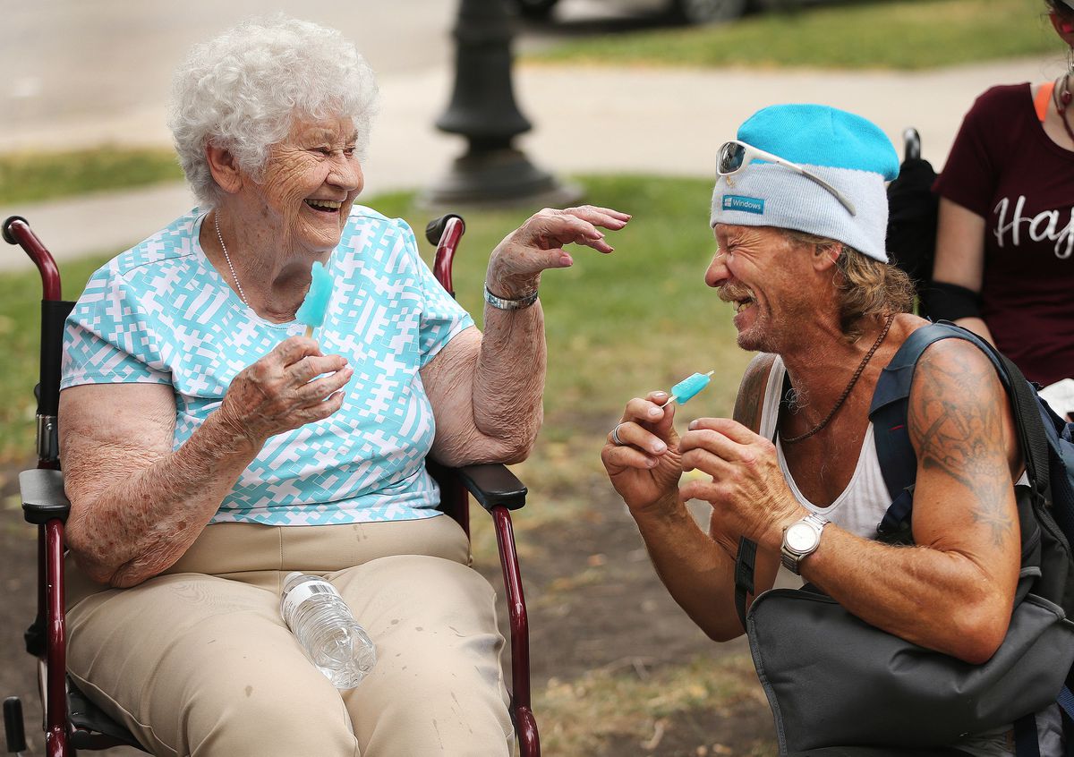 Donna Adams laughs as she shares her Popsicle with Scott Silcox, who is homeless, as senior residents from assisted living communities offer homeless people water, popsicles and candy on National Cheer Up the Lonely Day at Pioneer Park in Salt Lake City o
