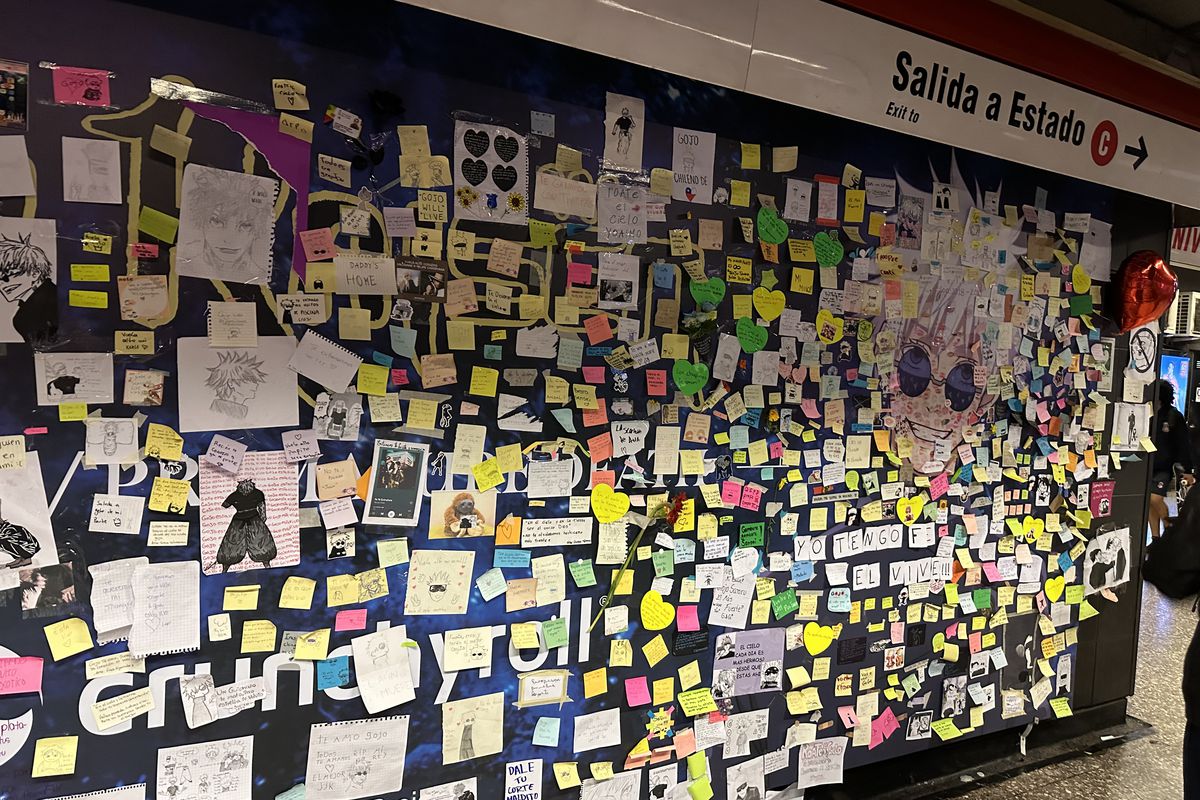 A photo of a Crunchyroll ad on a subway in Chile. The ad shows Gojo from Jujutsu Kaisen. The ad have been covered with notes and fan art dedicated to the character.