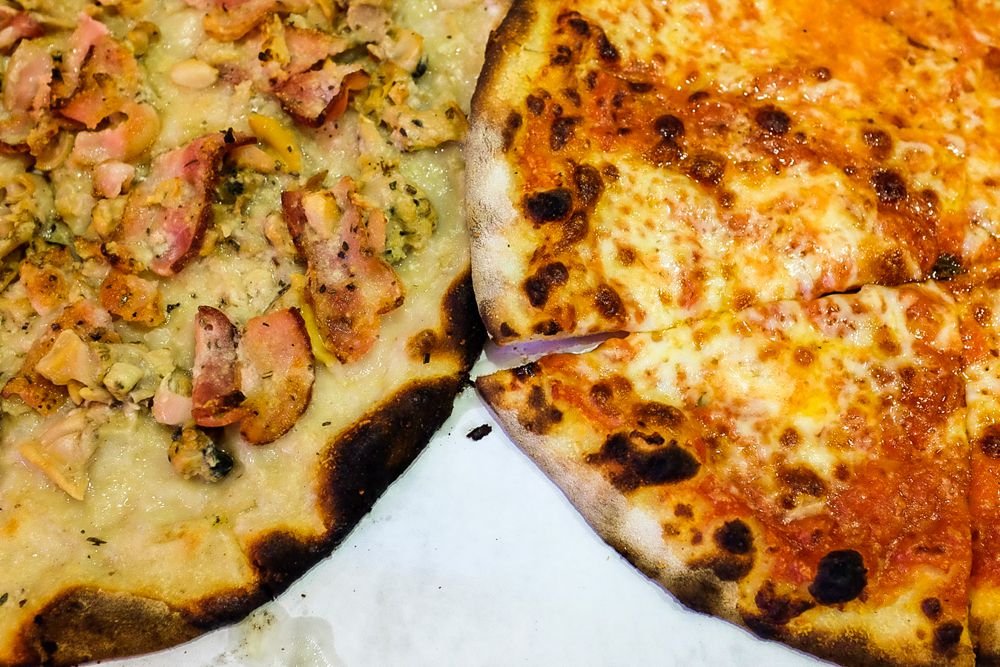 Overhead view of two New Haven-style pizzas with charred crust. One is topped with clams.