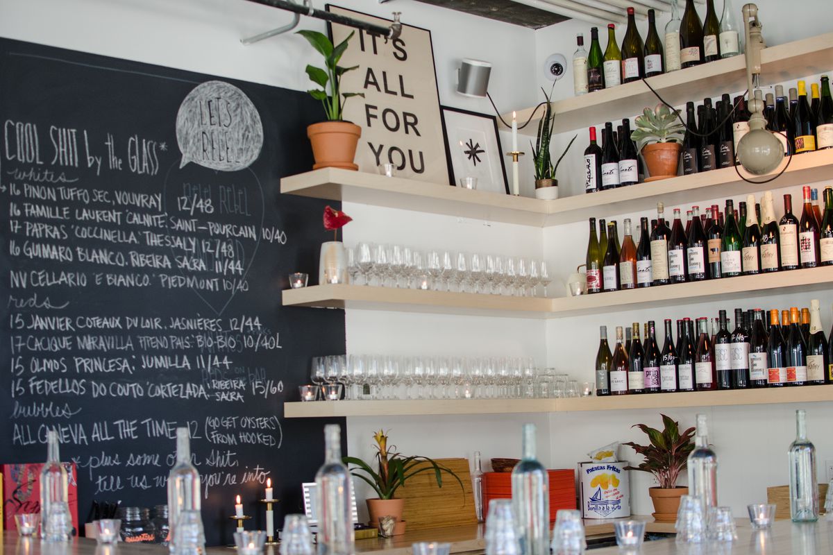 Shelves of wine bottles and a chalkboard menu inside a wine bar.