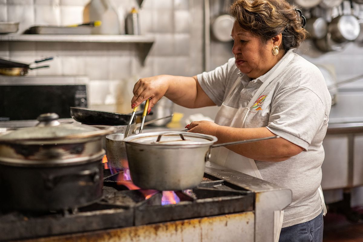 A woman works a busy kitchen stove inside a restaurant.