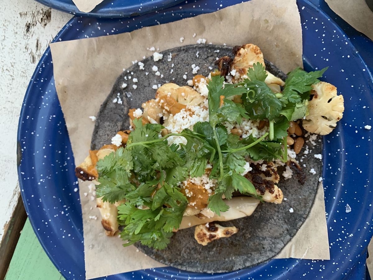 A blue tortilla topped with cauliflower and cilantro.