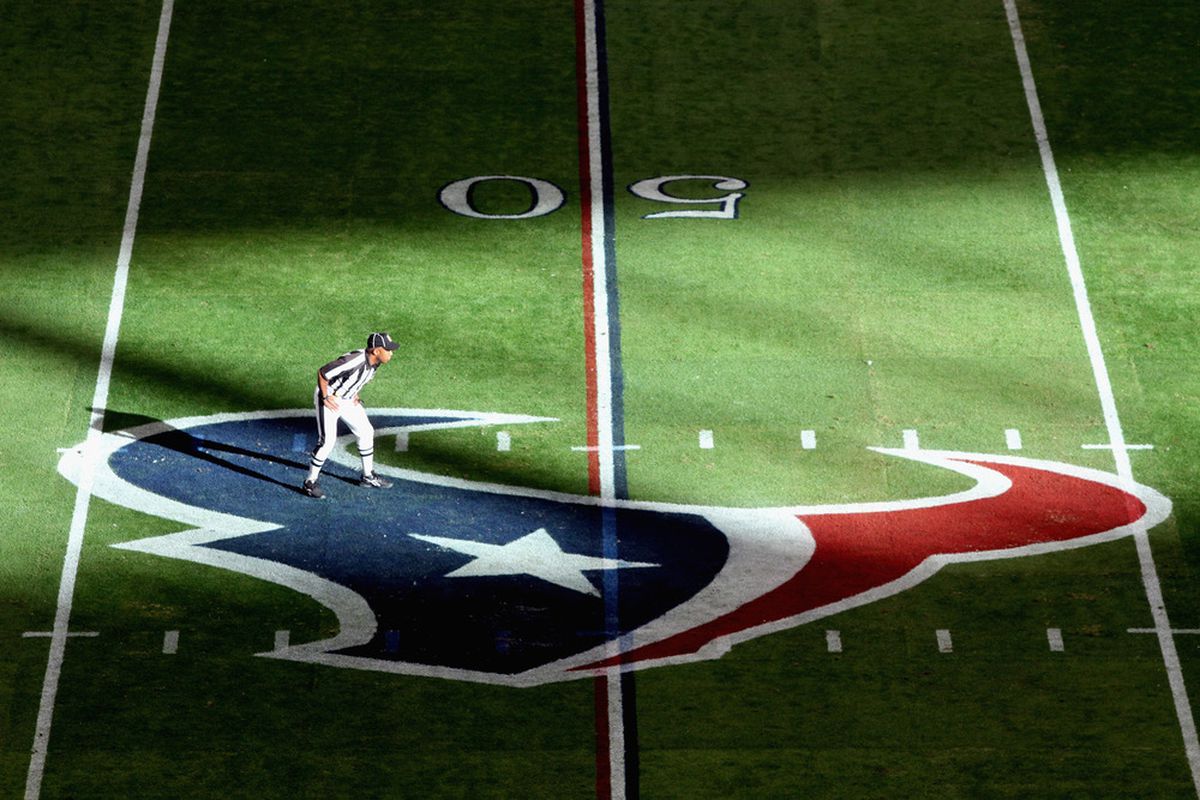 A referee is seen standing on a Houston Texans logo.