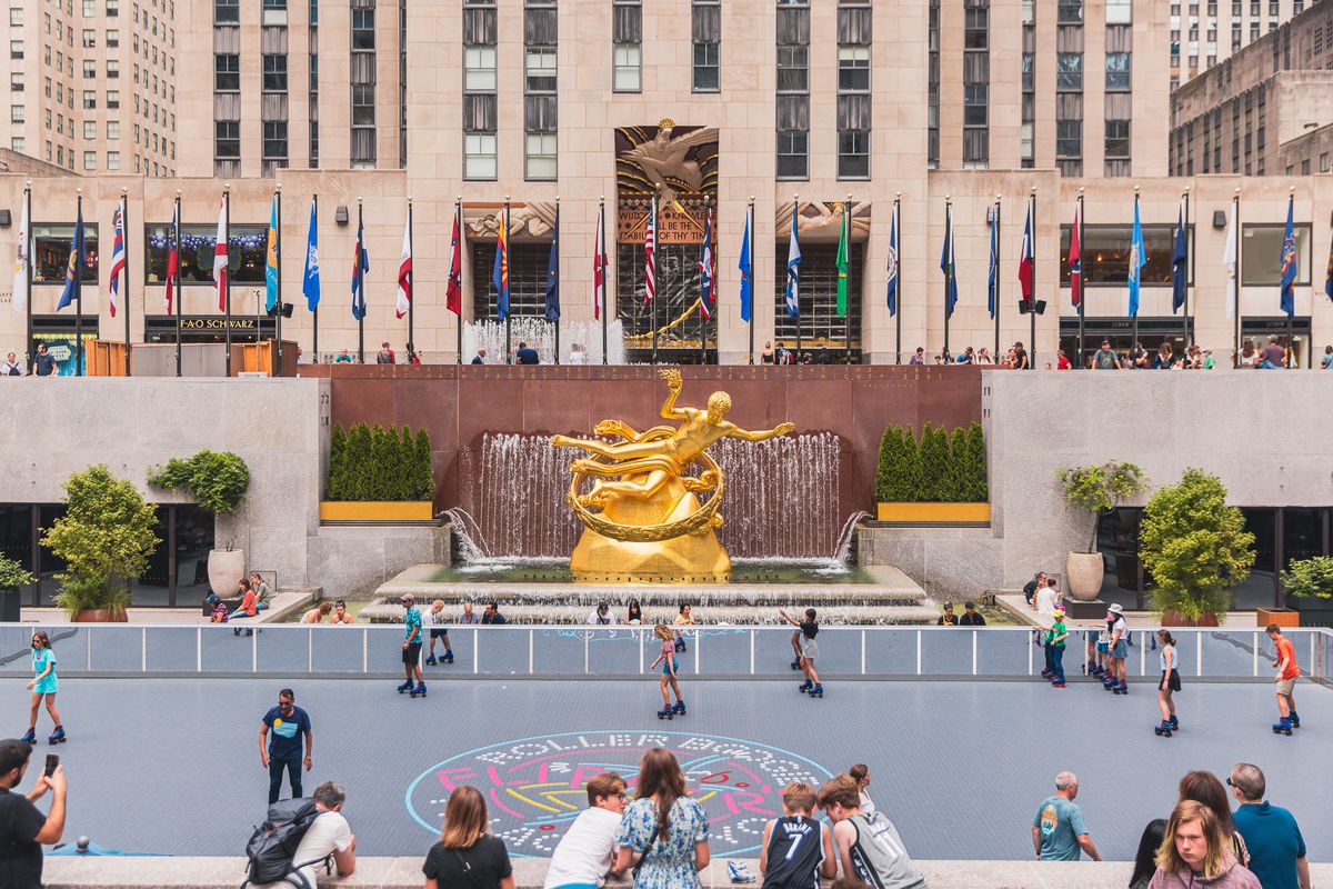 A golden statue overlooks a roller rink with people rollerblading and sitting on the sidelines at Rockefeller Center.