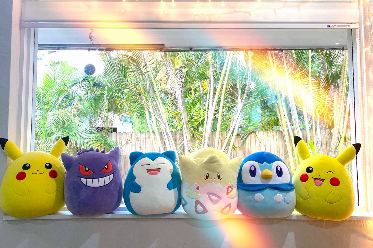 A lineup of Pokémon Squishmallows for Pikachu, Gengar, Snorlax, Togepi, Piplup and winking Pikachu sitting on a window sill