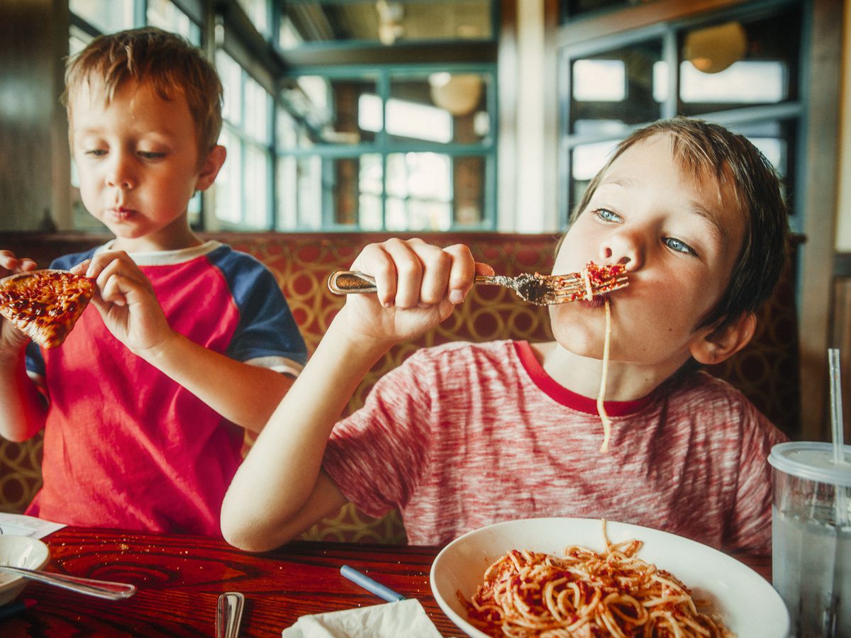 A picture of two kids eating pizza and spaghetti