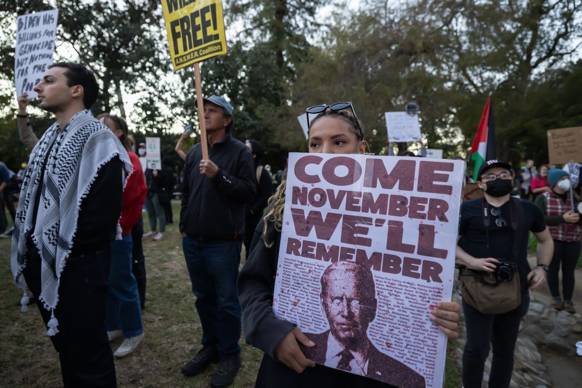 The protester holds a sign that says “Come November we’ll remember” with a picture of Biden beneath.